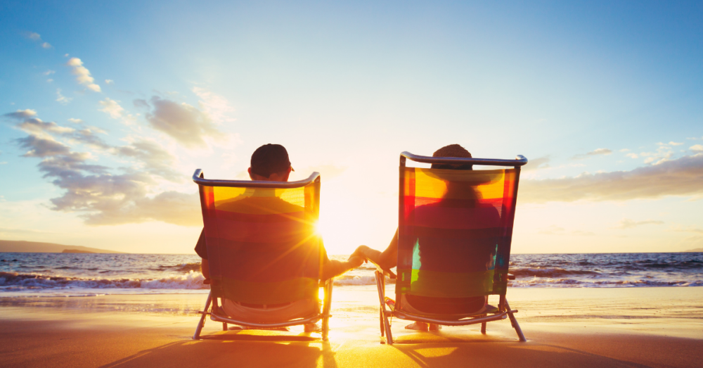 man and woman holding hands in beach chairs on the sand during sunset